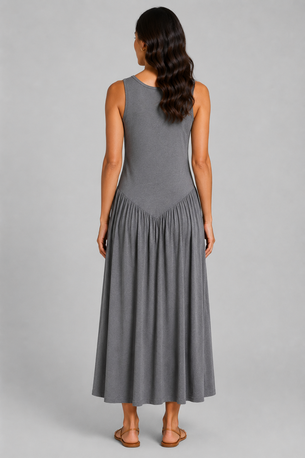 Women's sleeveless maxi dress featuring a scoop neckline, fitted bodice, and flowing gathered skirt. Shown in a soft brown jersey fabric with a relaxed silhouette and maxi length, styled on a model against a light grey studio background.