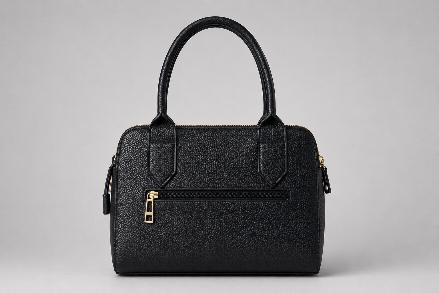 The Chelsea Tote Bag in Black featuring a structured design, pebbled faux leather finish, double zip compartments, gold-tone hardware, and embossed logo detail on a light grey studio background.