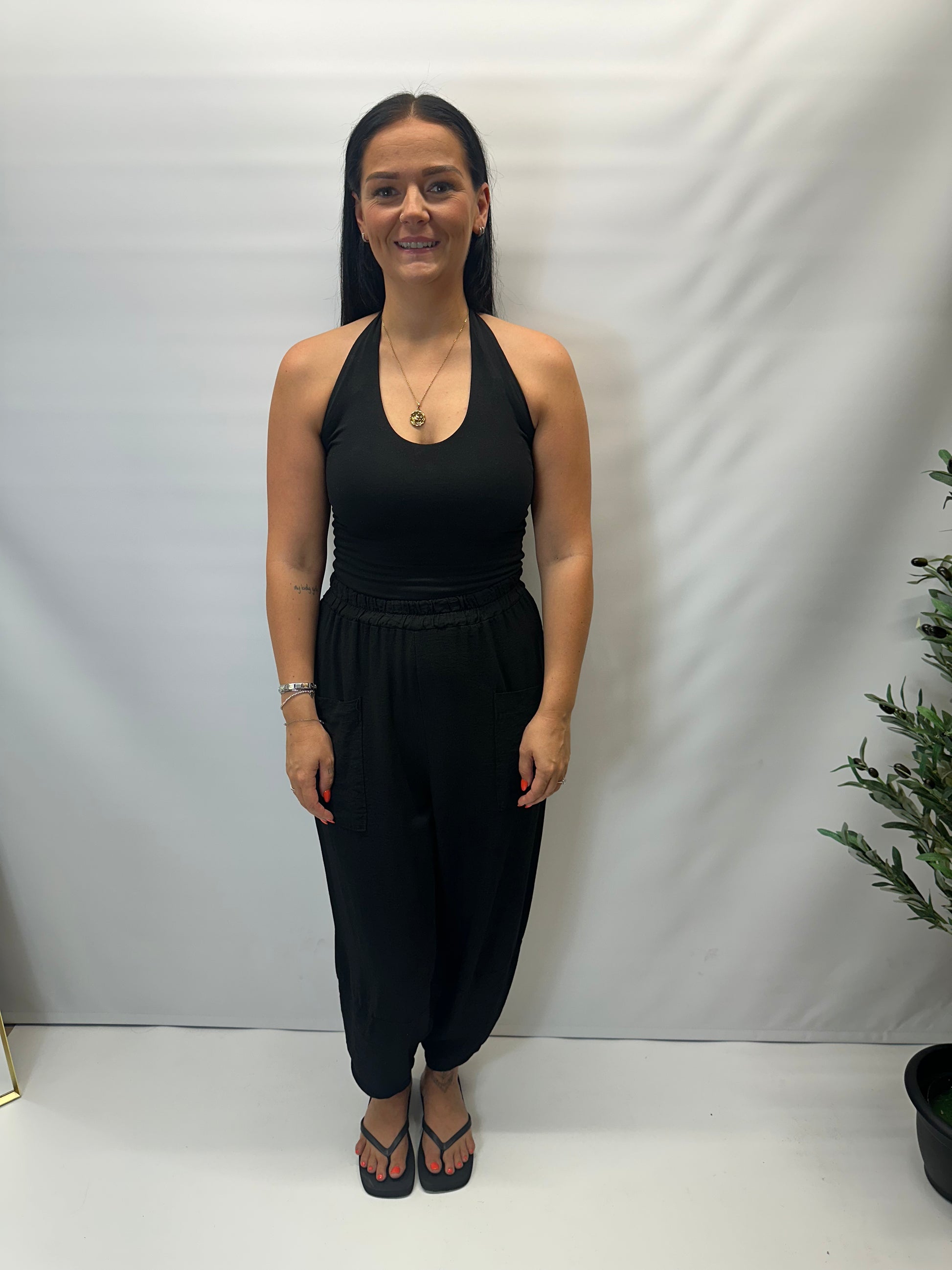 Model wearing black Italian relaxed tapered trousers with an elasticated waistband, front patch pockets and crossover split hem detail.