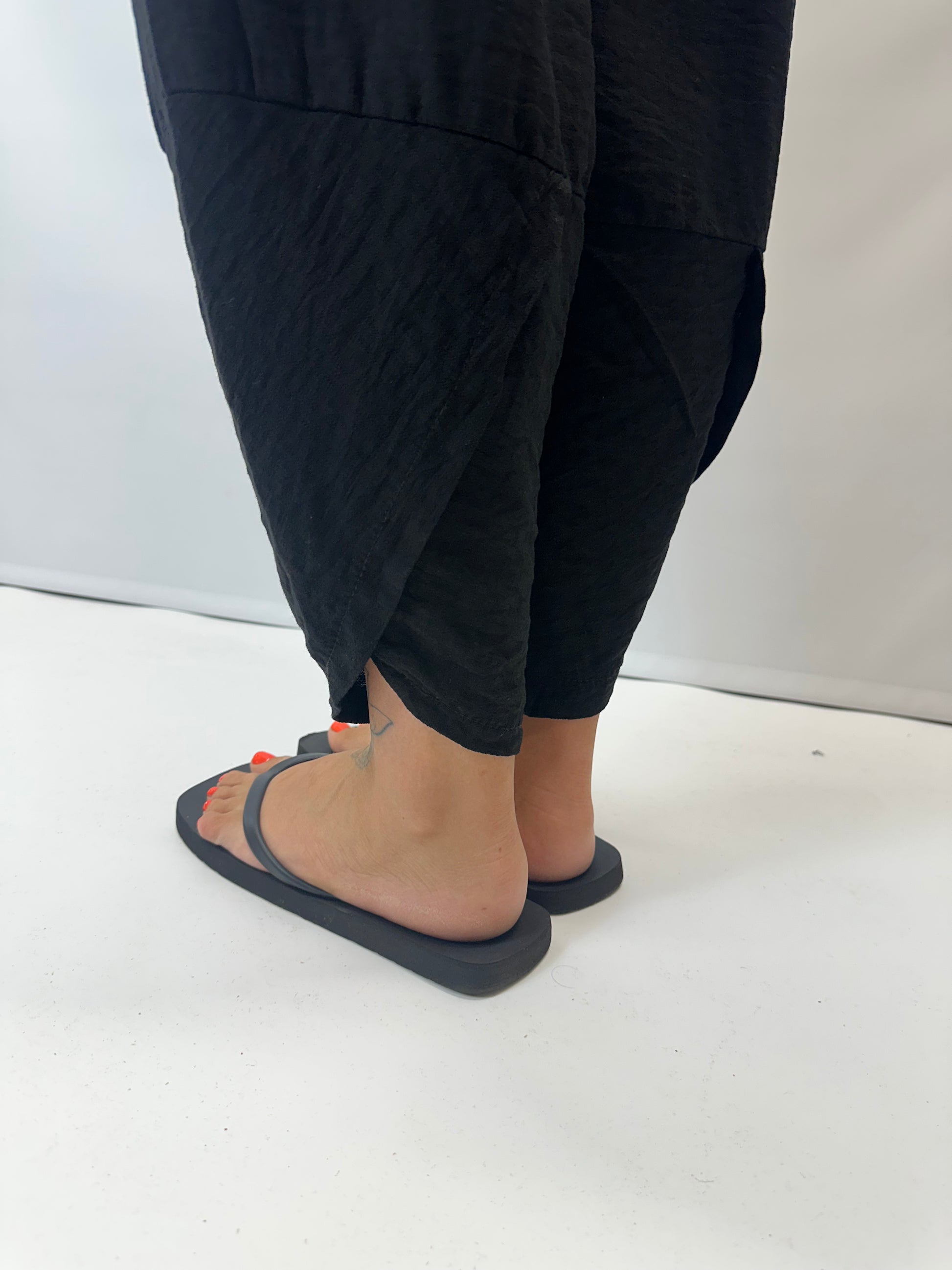Model wearing black Italian relaxed tapered trousers with an elasticated waistband, front patch pockets and crossover split hem detail.