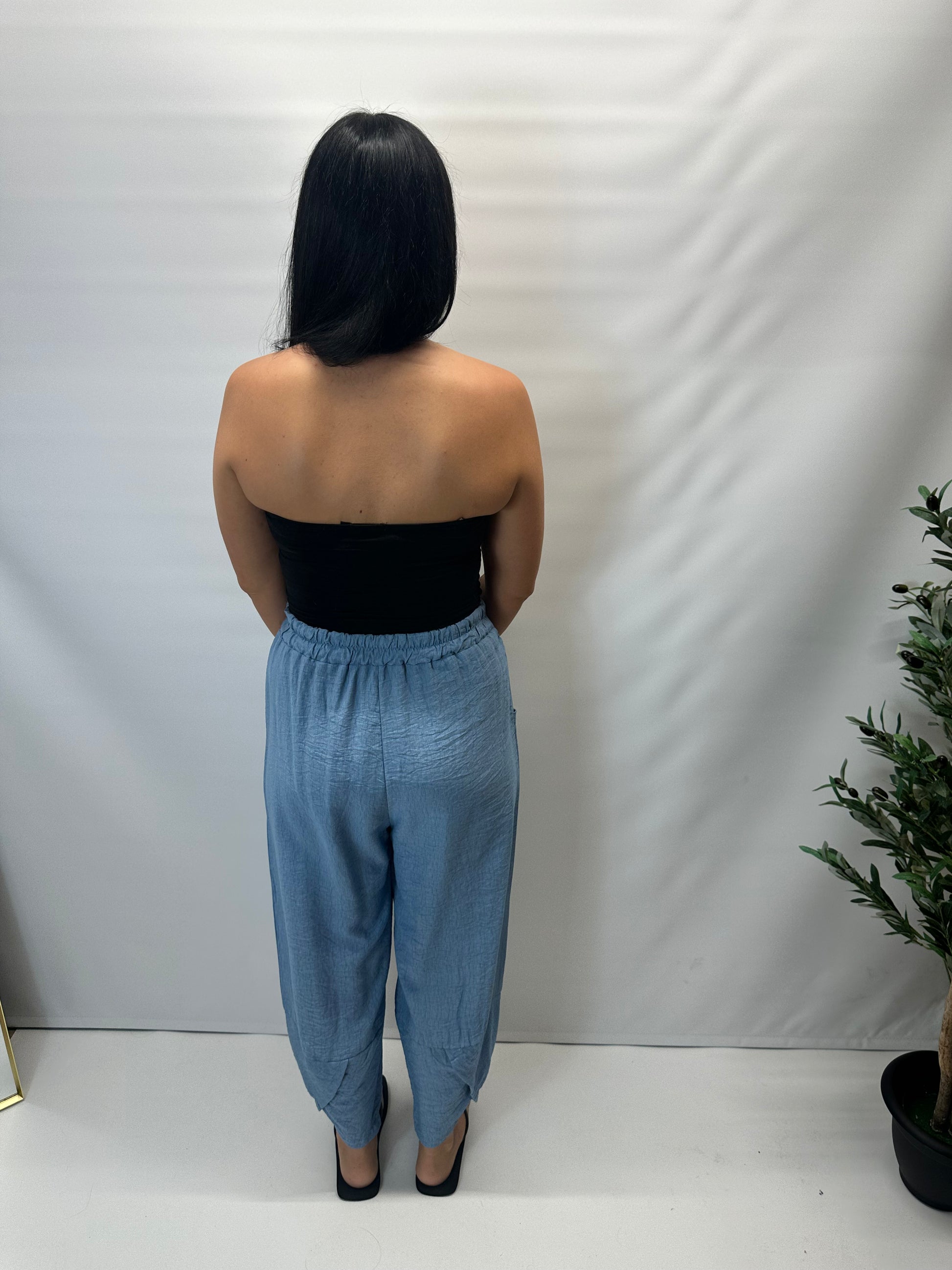 Model wearing black Italian relaxed tapered trousers with an elasticated waistband, front patch pockets and crossover split hem detail.