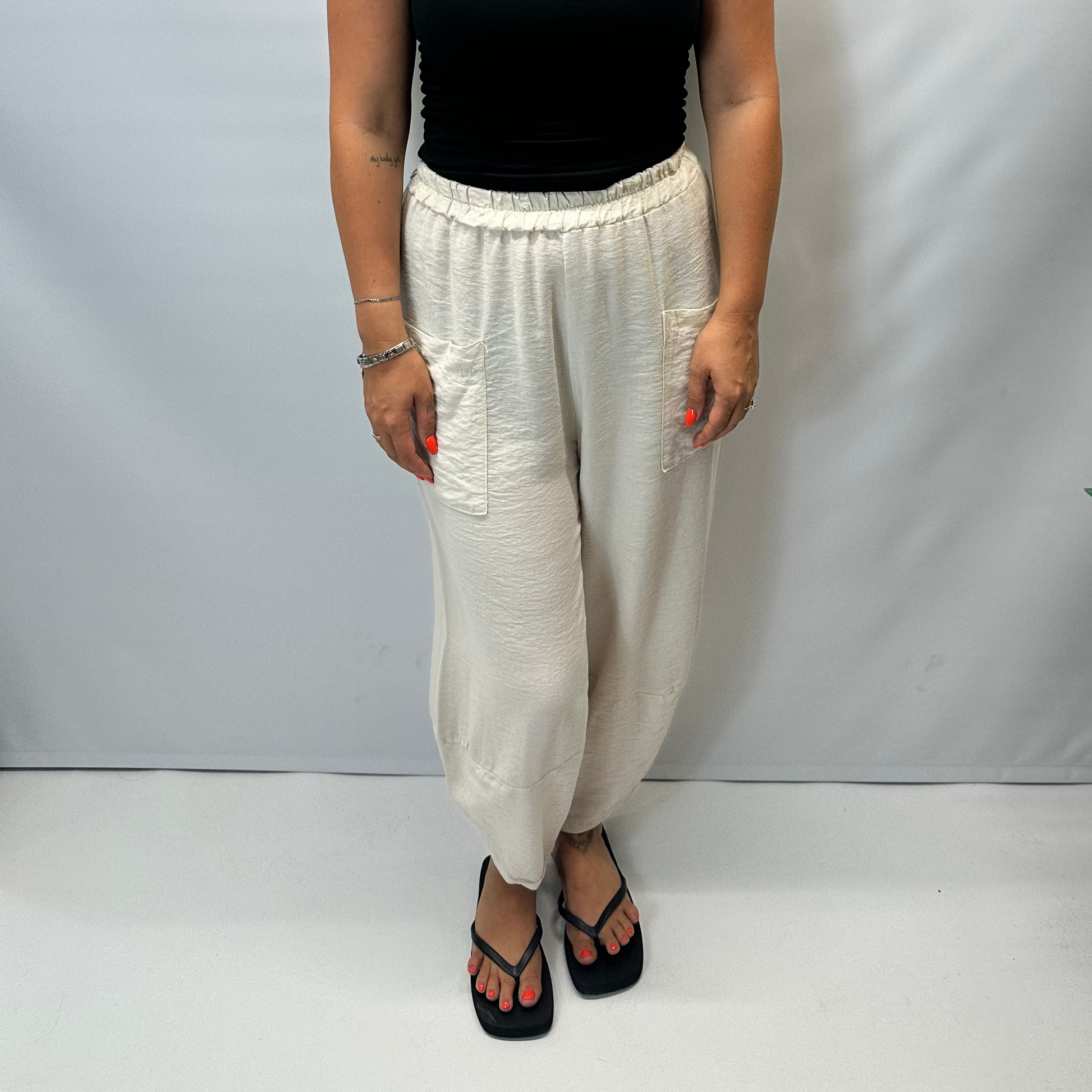 Model wearing beige Italian relaxed tapered trousers with an elasticated waistband, front patch pockets and crossover split hem detail.