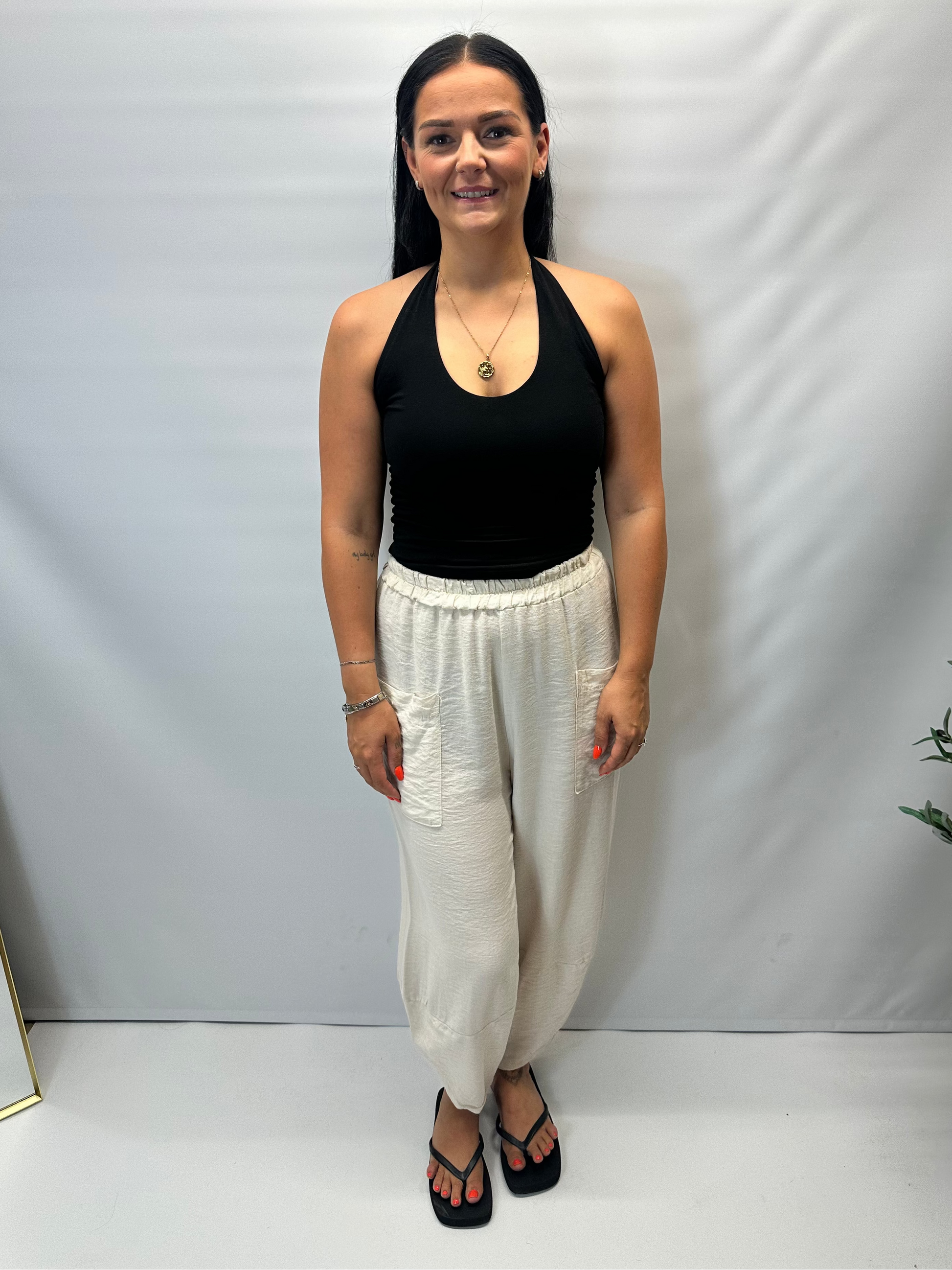 Model wearing beige Italian relaxed tapered trousers with an elasticated waistband, front patch pockets and crossover split hem detail.