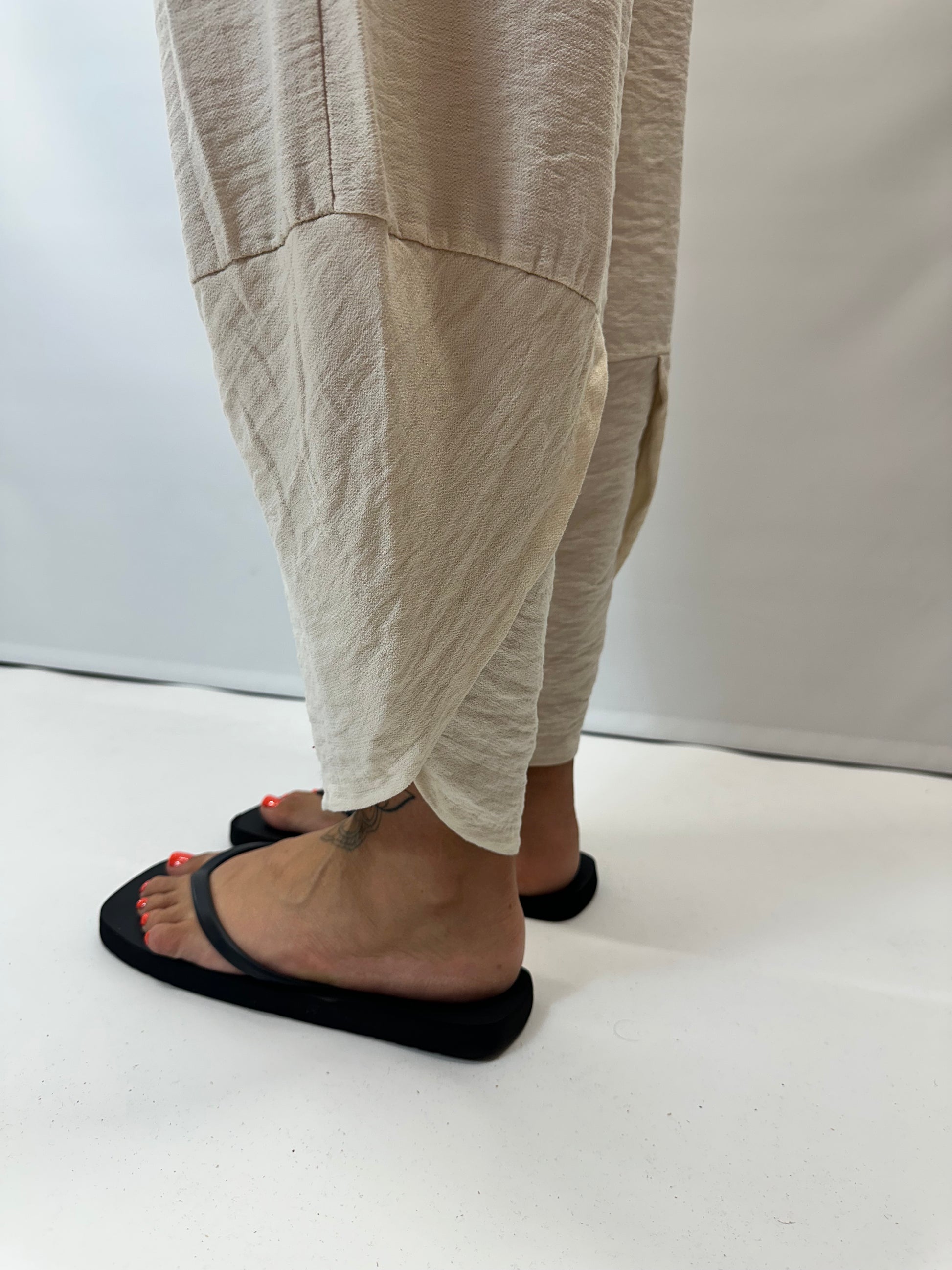 Model wearing beige Italian relaxed tapered trousers with an elasticated waistband, front patch pockets and crossover split hem detail.