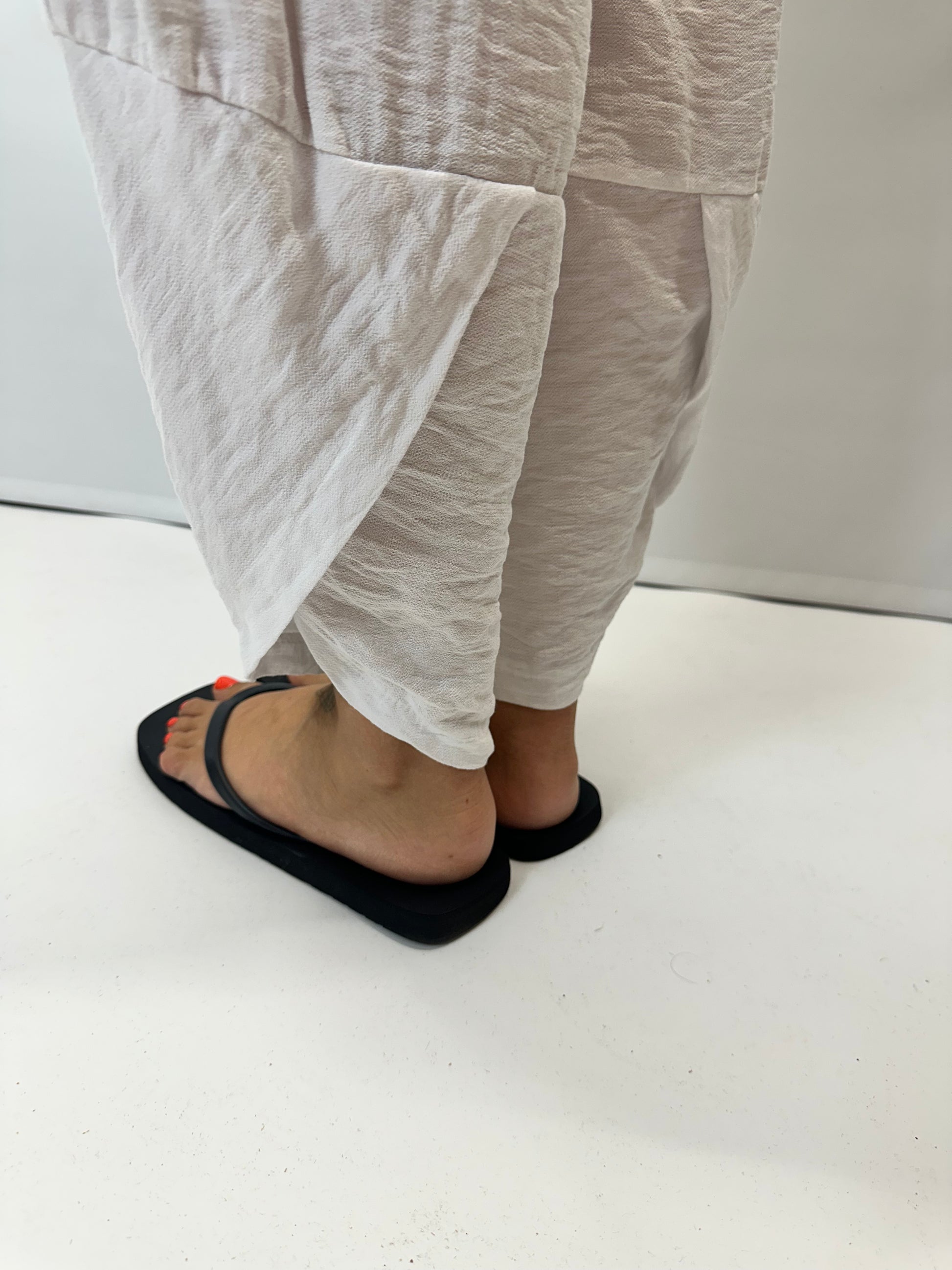 Model wearing white Italian relaxed tapered trousers with an elasticated waistband, front patch pockets and crossover split hem detail.
