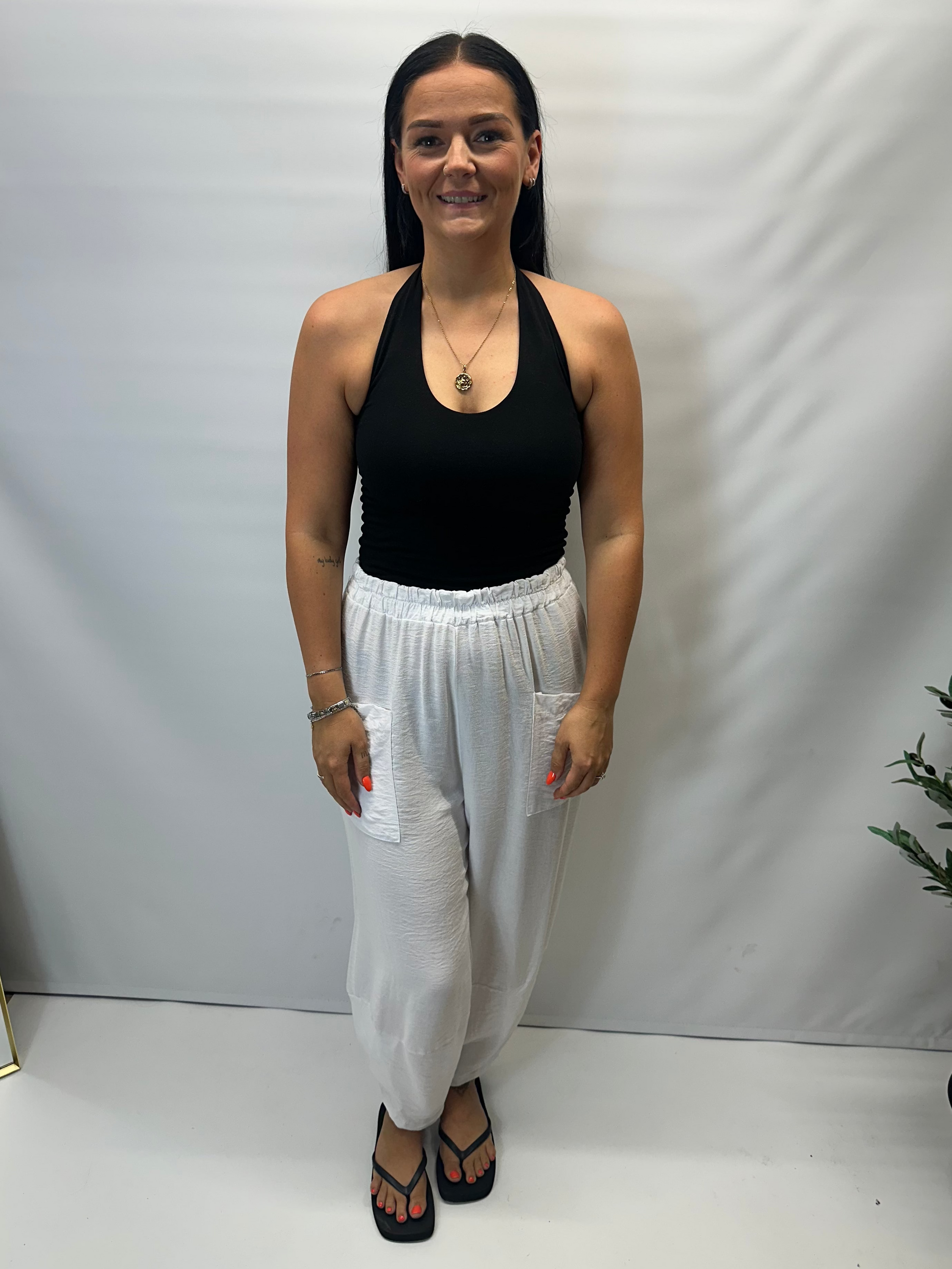 Model wearing white Italian relaxed tapered trousers with an elasticated waistband, front patch pockets and crossover split hem detail.